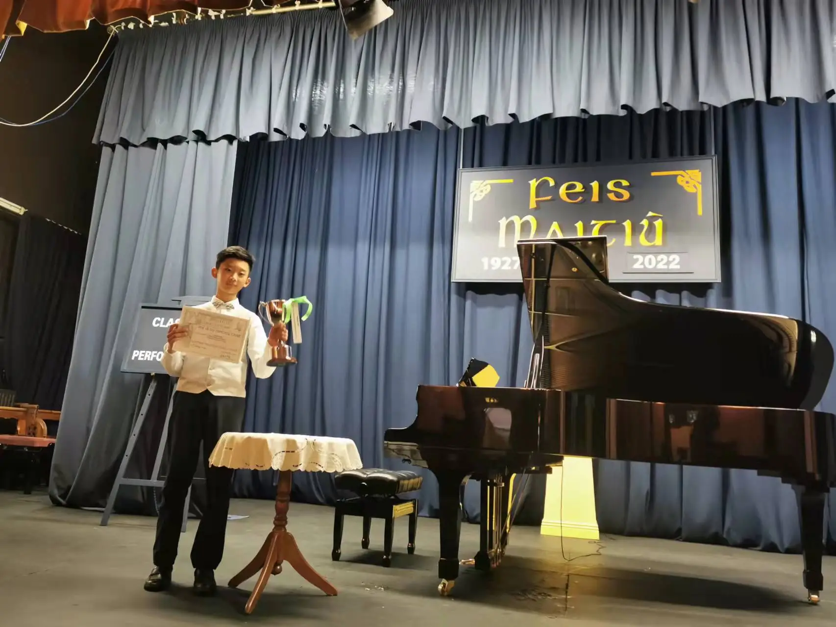 A student taking a bow on stage, trophy on the piano behind