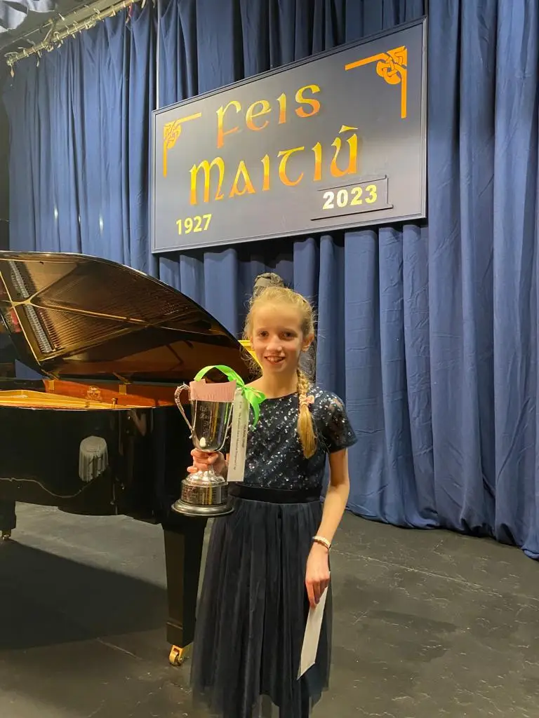 A student holding a trophy on stage at Feis Maitiú