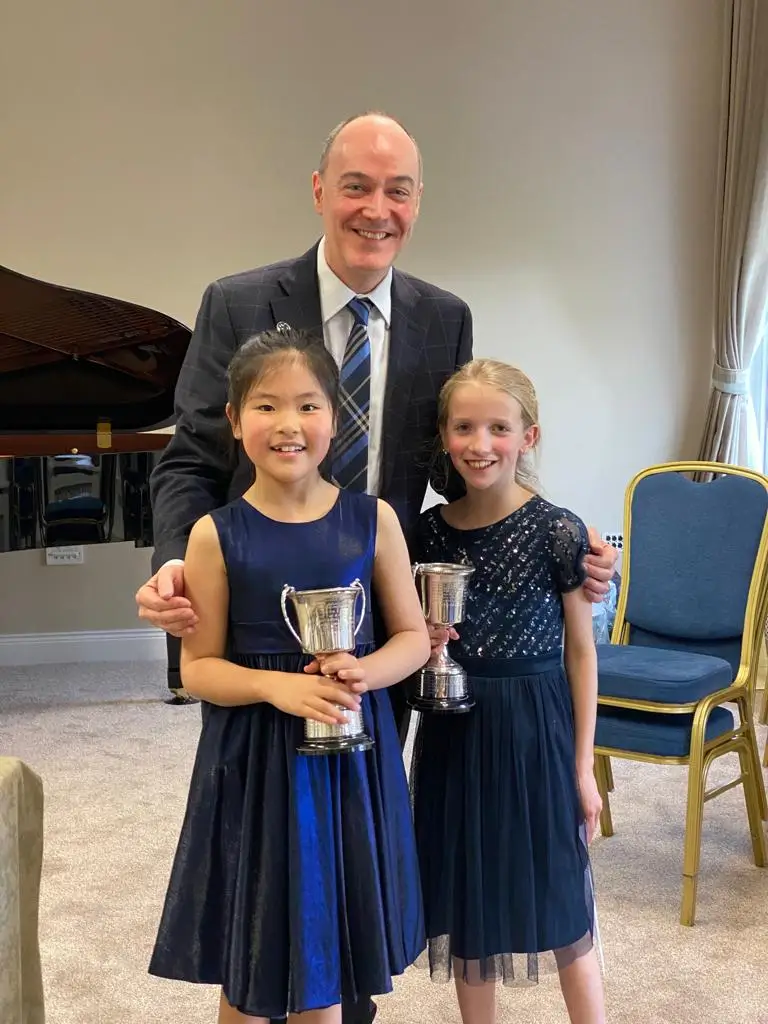 Two students with the adjudicator after their class, one holding a trophy